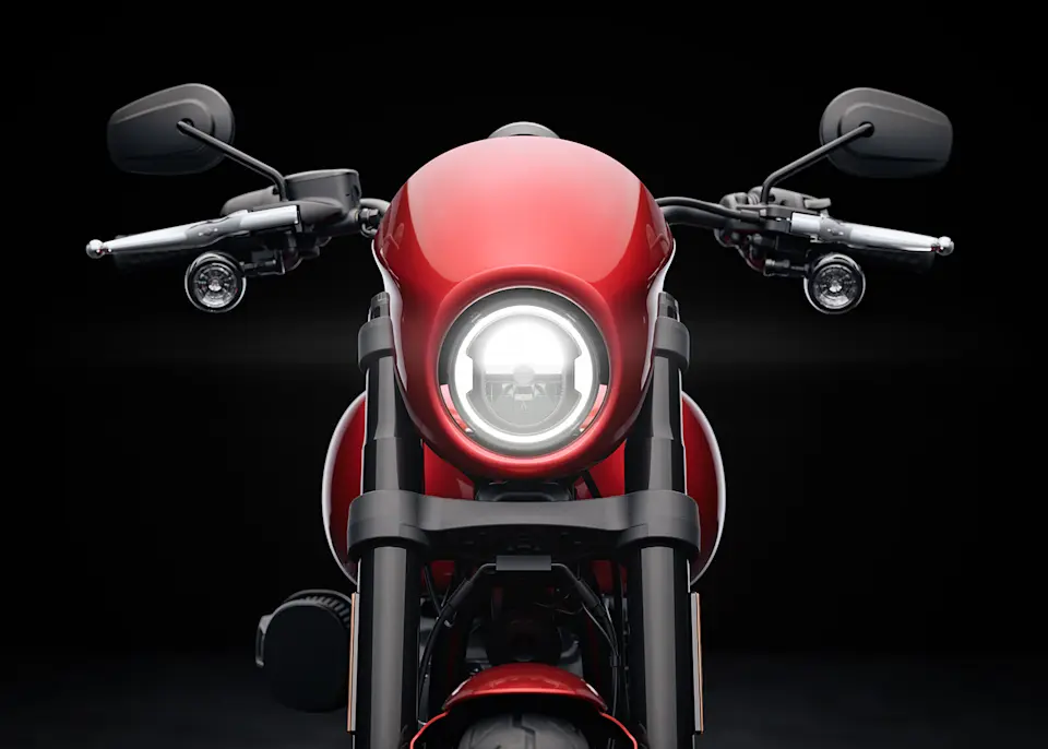 Bild des markanten Vorderrads einer roten Harley-Davidson Low Rider S mit einem leuchtenden Scheinwerfer vor schwarzem Hintergrund.