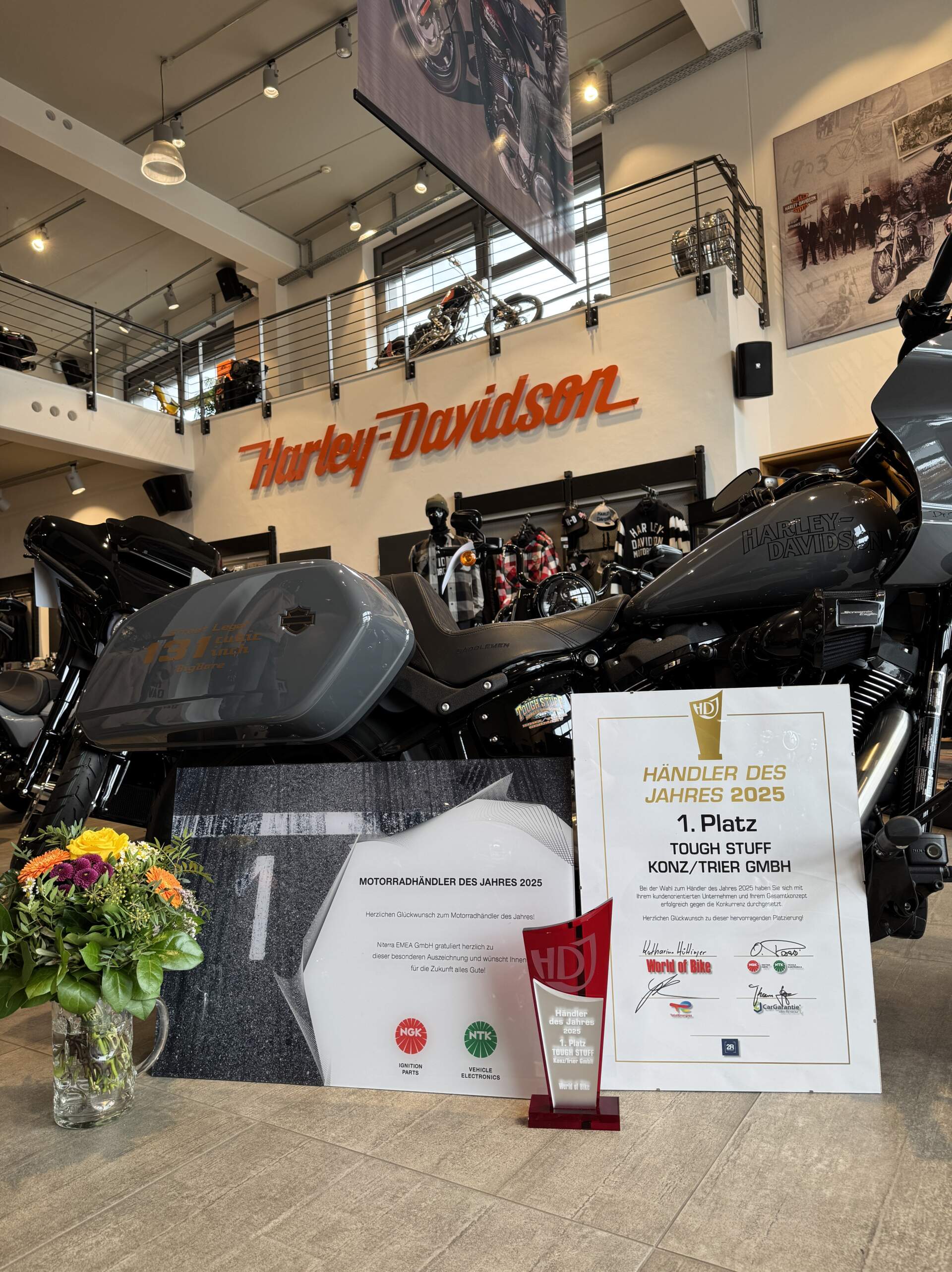 Mehrere Ausführungen der Auszeichnung "Händler des Jahres" stehen vor einem grauen Harley-Davidson Motorrad