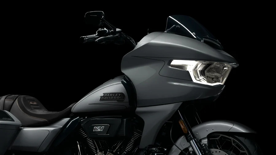 Die Abbildung zeigt die elegante Frontansicht eines Harley-Davidson Motorrads in grau mit markantem Scheinwerfer und minimalistischer Verkleidung vor schwarzem Hintergrund.