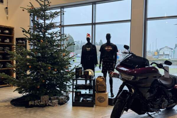 Ein geschmückter Weihnachtsbaum in einem Harley-Davidson Store neben zwei Schaufensterpuppen in H-D Kleidung und einem H-D Road Glide Motorrad auf einem mit Lichterketten geschmücktem Podest