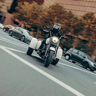 Ein Fahrer auf einem Harley-Davidson Freewheeler fährt mit Schwung über eine Straße, umgeben von anderen Fahrzeugen.
