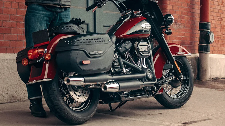 Eine rot-schwarze Harley-Davidson-Maschine steht an einer Wand, während eine Person mit einem Bein neben ihr steht.