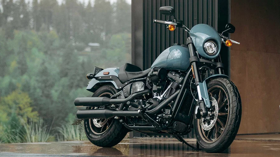 Eine Harley-Davidson Motorrad in mattem Blau steht in einem modernen Umfeld mit grüner Natur im Hintergrund.