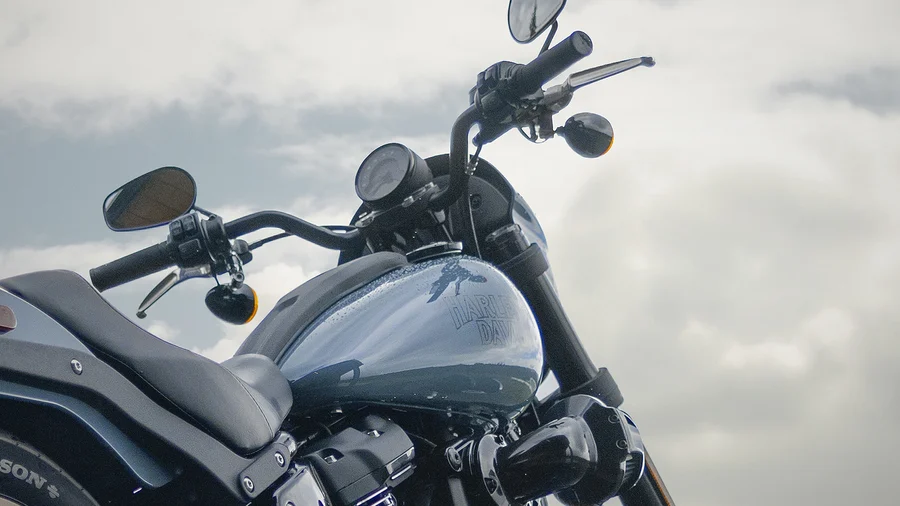 Detailaufnahme eines Harley-Davidson Motorrads, die den Lenker, das Cockpit und den blauen Tank zeigt, vor einem bewölkten Himmel.