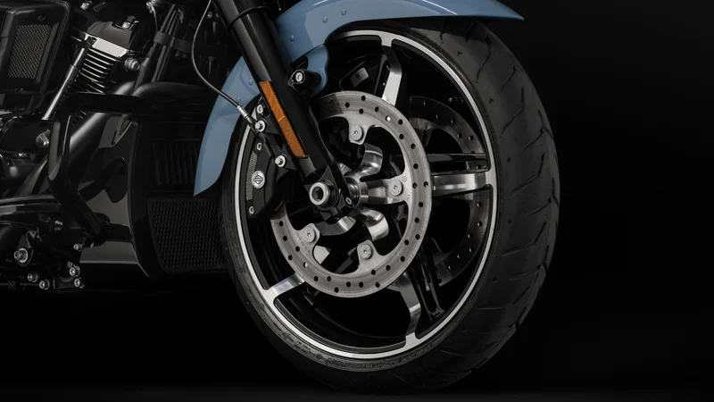 Detailaufnahme des Vorderrads einer Harley-Davidson mit modernen Speichen und einer breiten Bereifung vor schwarzem Hintergrund.