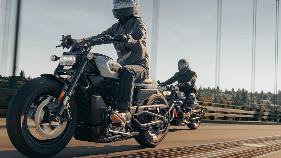 Zwei Motorradfahrer auf Harley-Davidson Motorrädern fahren über eine Brücke.